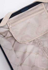 Beige travel bag interior featuring a mesh pocket, smooth lining with repeated logo pattern, and a zipper closure along the top edge.