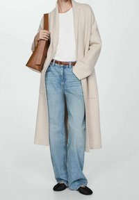 Beige pitkä neuletakki valkoisen t-paidan päällä, yhdistetty vaaleansinisiin väljälahkeisiin farkkuihin ja mustiin tasapohjaisiin kenkiin. Ruskea käsilaukku korostaa asua.