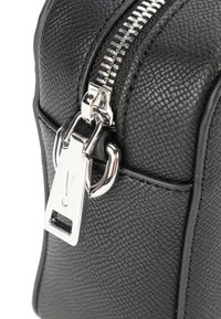 Schwarze Lederhandtasche mit strukturierter Oberfläche, ausgestattet mit einem silbernen Reißverschluss und Hardware, hervorgehoben durch ein markantes Metallschild am Reißverschluss. 