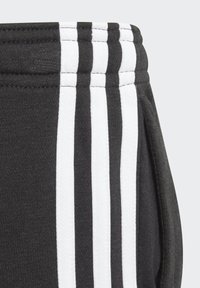 Pantalones deportivos negros con rayas verticales blancas, textura suave, cintura acanalada y bolsillos laterales, adecuados para ropa activa.