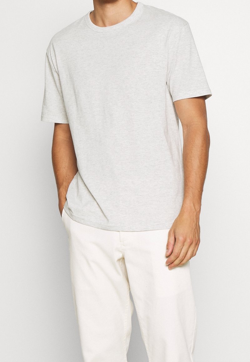 Lichtgrijze katoenen t-shirt met een ronde hals en korte mouwen, met een losse pasvorm en een gladde textuur, gedragen met crèmekleurige broeken.