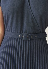 Dunkelblaues Jeanskleid mit einem gefältelten Rock, passendem Stoffgürtel mit rechteckiger Schnalle und einer weichen, texturierten Oberfläche.