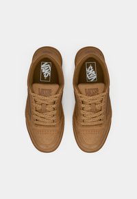 Sneaker in suede marrone con punta forata, lacci abbinati e logo Vans sulla linguetta. Suola piatta con leggera elevazione nel tallone.