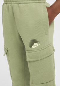 Pantaloni cargo verdi in morbido cotone misto, con tasche laterali e un piccolo logo Nike bianco sulla coscia con effetto ombra.