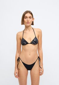 Μαύρο μπικίνι σετ με τριγωνικό τοπ με γεωμετρικό σχέδιο και ρυθμιζόμενα κάτω μέρη που δένουν στο πλάι. Μαλακή υφή, μινιμαλιστικός σχεδιασμός.