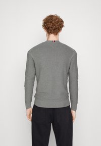 Pull gris tricoté avec un col rond et des poignets côtelés, présentant un petit détail rouge, blanc et bleu à l'arrière du col.