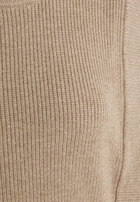 Tissu en tricot beige avec une texture côtelée. Le matériau semble doux, avec une transition sans couture vers une section légèrement plus lisse à droite.