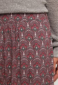 Sukně s vzorem, která se vyznačuje odvážným designem s červenými, zelenými a bílými květinovými motivy na tmavém pozadí. Vyrobena z lehkého materiálu, má řasený pas.