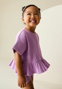 Liliowy prążkowany top z krótkimi rękawami, z falbanką na dole. Połączony z wzorzystymi szortami, prezentującymi zabawny design. Gładka faktura.