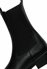 Botte Chelsea en cuir noir avec panneau latéral élastique et languette, présentant un talon empilé bas et une finition lisse.