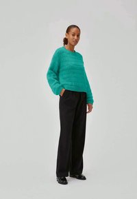 Maglione lavorato a maglia di colore verde acqua con finitura testurizzata e scollatura rotonda, abbinato a pantaloni neri a vita alta e scarpe nere.
