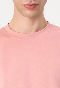 Φωτεινό ροζ μπλουζάκι με στρογγυλή λαιμόκοψη, φτιαγμένο από μαλακό και λεία ύφασμα. Διαθέτει ελαφρώς υφαντή επιφάνεια και απλές, καθαρές γραμμές.