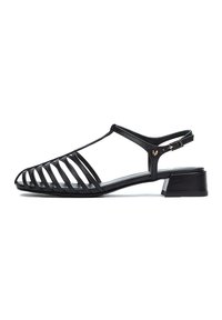 Sandalias negras con diseño abierto y ranurado, hechas de piel suave, con un tacón bajo y una correa ajustable con hebilla. Suela plana.
