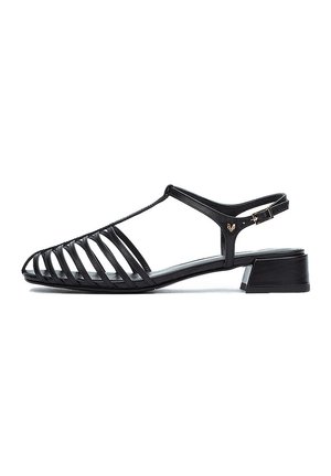 Sandalias negras con diseño abierto y ranurado, hechas de piel suave, con un tacón bajo y una correa ajustable con hebilla. Suela plana.