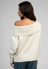 Pull crème à épaules dénudées avec texture côtelée et col large, aux manches amples et à l'ourlet droit, porté avec un jean.