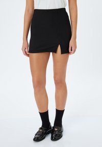 Minifalda negra acanalada con una abertura lateral, diseñada para una silueta ajustada. Combinada con zapatos de loafer negros y calcetines. Textura suave.