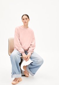 Ljusrosa oversized sweatshirt med sänkta axlar, kombinerad med lösa ljusblå jeans och kraftiga ljusrosa sneakers. Minimalistisk design.
