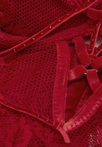 Rød lingeri med blonder og mesh, med en blød tekstur. Remme prydet med røde perler og et lagdelt design skaber visuel interesse.