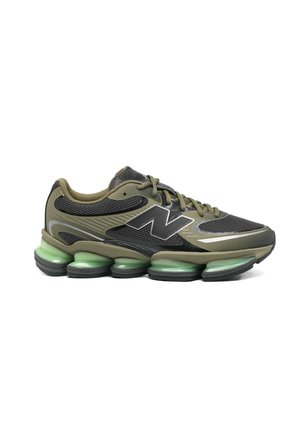 Zapatilla deportiva verde oliva y negra con cordones, parte superior de malla, gran logotipo "N" y suela acolchada segmentada distintiva con tono verde.