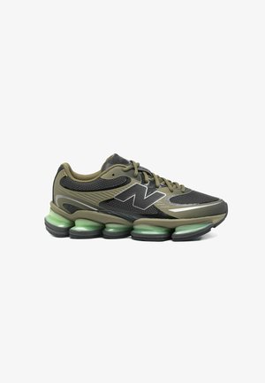 Zapatilla deportiva verde oliva y negra con cordones, parte superior de malla, gran logotipo "N" y suela acolchada segmentada distintiva con tono verde.