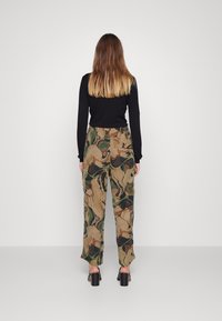 Blusa de manga longa preta e calças cargo estampadas em tons terrosos de castanho, verde e bege, com um corte folgado e bolsos laterais.