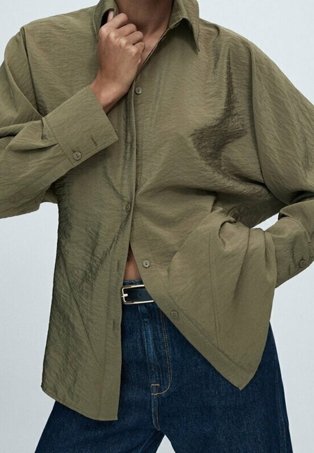 Olivgrön skjorta med knappar och avslappnad passform, med en texturerad tyg, långa ärmar och ett subtilt skrynklat mönster. Bärs över mörk denim.