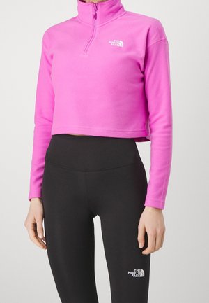 Person wearing a bright pink cropped fleece pullover and black high-waisted leggings, both with The North Face logo.