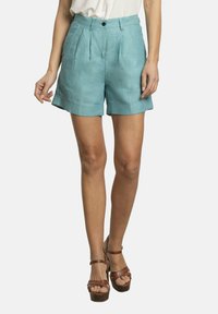 Bermudas de lino azul claro con un corte a medida, que presentan pliegues y dobladillos doblados. Llevadas con sandalias de plataforma marrones.