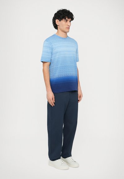 Zils gradienta T-krekls ar horizontālām svītrām, īsām piedurknēm, apaļu kaklu, kopā ar tumši ziliem biksēm un baltiem sporta apaviem.