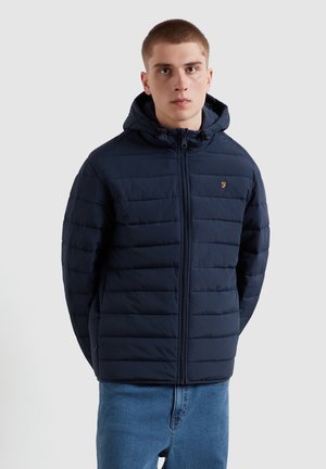 Marineblauwe pufferjack met een capuchon, voorzien van horizontale quilting en een ritssluiting. Klein logo in goud op de linkerborst. Gemaakt van lichtgewicht materiaal.
