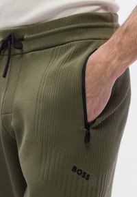 Pantalones jogger verde oliva con tejido de punto texturizado, que cuentan con un bolsillo con cremallera y cordón negro, con un discreto logo 'BOSS'.