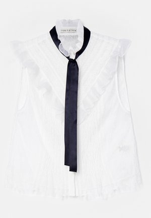 Witte mouwloze blouse met ruches en een donkerblauwe satijnen strik bij de hals. Geweven stof met een delicaat patroon.