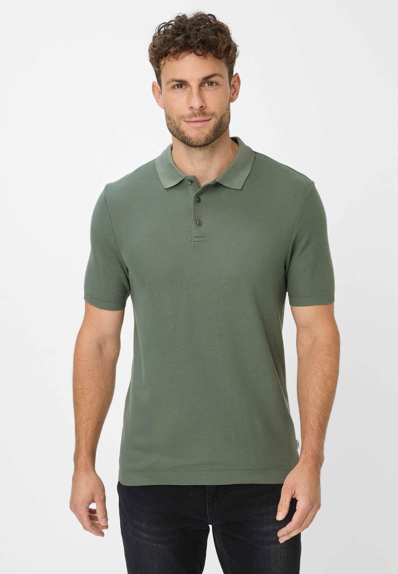 Grøn kortærmet polo skjorte lavet af struktureret stof, med krave og tre-knap lukning, parret med mørke jeans.