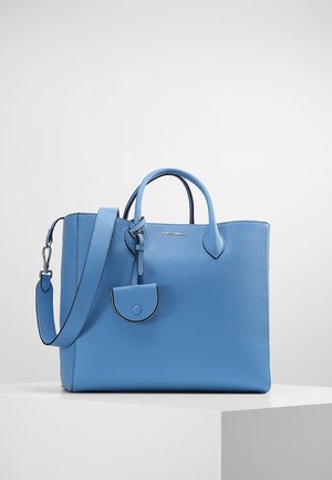 Sac à main en cuir bleu avec doubles poignées, bandoulière amovible et petite pochette attachée sur une surface blanche unie.
