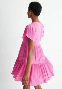 Vestido rosa con pliegues, mangas cortas con volantes, un corsé ajustado y una falda acampanada. El material parece suave y ligero, con un patrón texturizado.