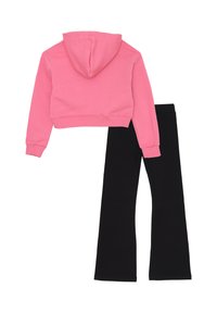 Felpa rosa tagliata con cappuccio e maniche lunghe abbinata a leggings neri a campana, entrambi realizzati in materiale morbido e elastico.