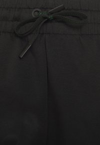 Pantaloni sportivi neri con vita regolabile, caratterizzati da un tessuto strutturato e accenti di cucitura verde vicino al cordoncino.