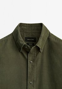 Chemise en velours côtelé vert olive à boutons, avec col boutonné et étiquette de marque visible à l'intérieur du col.