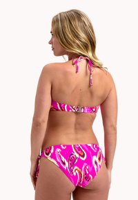 Bikini rose avec un motif paisley, bretelles à nouer derrière le cou, un fermoir à l'arrière et un tissu texturé. Le bas est de coupe taille basse.