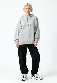 Pilkas didelis džemperis su kengūros kišeniu, gaučiais rankogaliais ir užtraukiama kapuce, derinamas su juodais krovinių kelniais ir baltais sportiniais bateliais.