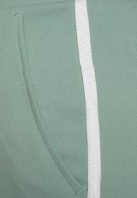 Hellgrüner Stoff mit einer strukturierten Oberfläche; verfügt über eine Seitentasche und einen weißen Akzentstreifen entlang des Randes.