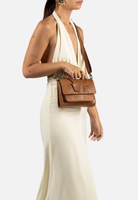 Borsa a tracolla in pelle marrone con una trama a coccodrillo, dotata di una tracolla removibile e accessori in metallo. Forma rettangolare compatta.
