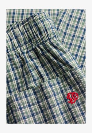 Grønt, blåt og hvidt ternet stof med elastisk linning og en rød broderet logo på en lomme.