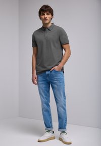 Polo gris à manches courtes, col plat et petit logo, associé à un jean en denim bleu clair et des baskets blanches avec des accents verts.