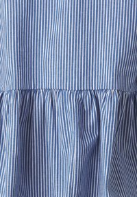 Μπλε και λευκό ριγέ ύφασμα με συ gathered ραφή στο κάτω μέρος, διαθέτοντας λεία υφή και ομοιόμορφο σχέδιο σε όλη την επιφάνεια.