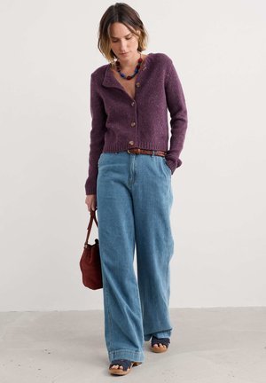 Purple wool cardigan with wooden buttons, paired with light blue high-waisted wide-leg denim pants. Brown braided belt and red bag.