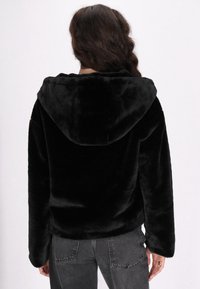 Hoodie in pelliccia sintetica nera con texture morbida, maniche lunghe e cappuccio ampio. La parte posteriore è senza cuciture, con una vestibilità comoda e senza dettagli metallici visibili.