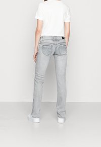 Grå denimjeans med rak bendesign, som har en medelhög midja och två bakfickor. I kombination med en vit t-shirt och vita sneakers.