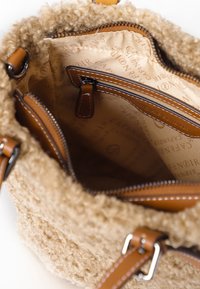 Interno della borsa morbido e texturizzato di colore beige, foderato con tessuto chiaro. Presenta scomparti con zip e dettagli in pelle marrone.
