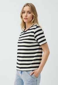 Top a maniche corte a righe bianche e nere con scollatura a girocollo. Tessuto morbido, vestibilità rilassata, abbinato a jeans in denim blu chiaro.